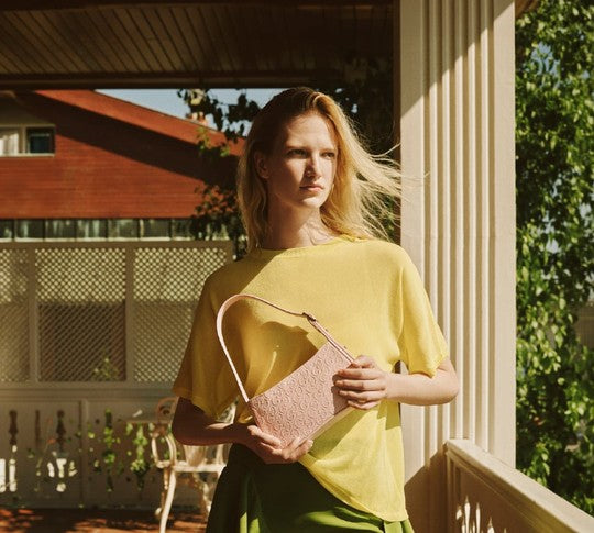 Woman in a yellow top carrying a woven raffia shoulder bag