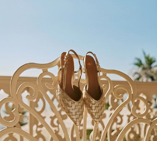 Two woven slingback shoes resting on an ornate garden bench